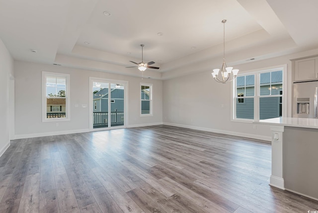 unfurnished living room featuring wood-type flooring, ceiling fan with notable chandelier, and a raised ceiling