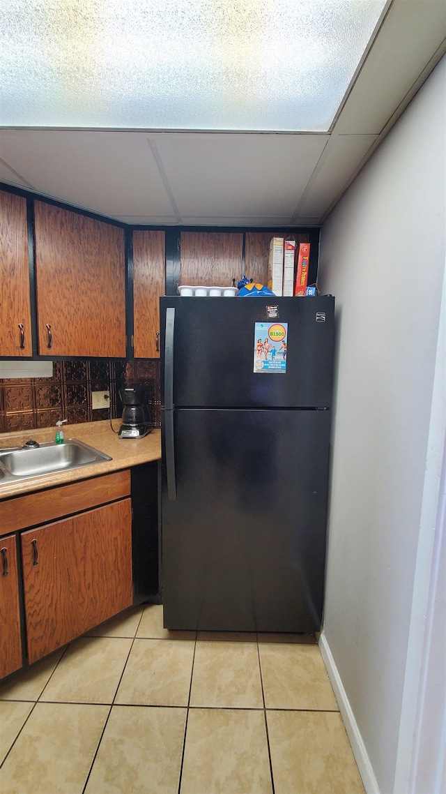 kitchen with a paneled ceiling, light tile floors, sink, and black fridge