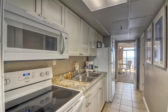 kitchen featuring white appliances, light tile patterned floors, sink, a paneled ceiling, and white cabinets