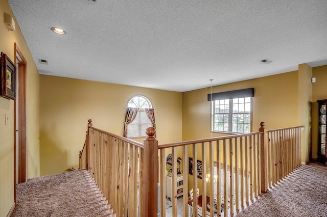 hallway with plenty of natural light, a textured ceiling, and carpet floors