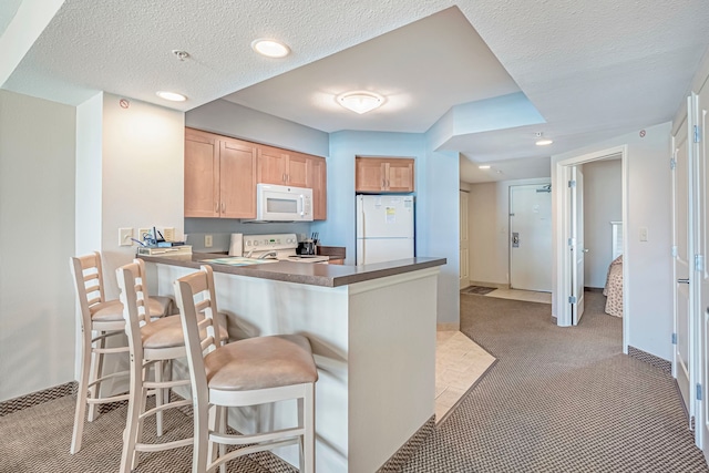 kitchen featuring light colored carpet, a textured ceiling, kitchen peninsula, a breakfast bar, and white appliances