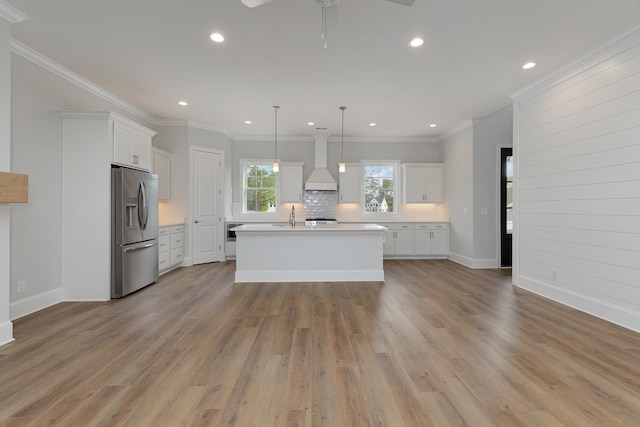 kitchen with white cabinets, pendant lighting, premium range hood, stainless steel fridge, and a kitchen island with sink