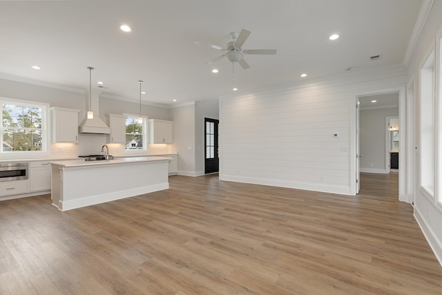 kitchen featuring a center island with sink, custom range hood, oven, white cabinetry, and decorative light fixtures