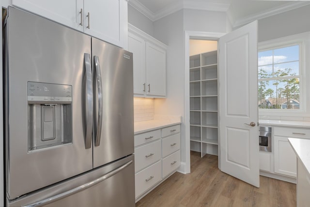 kitchen featuring stainless steel appliances, white cabinets, ornamental molding, light hardwood / wood-style floors, and decorative backsplash