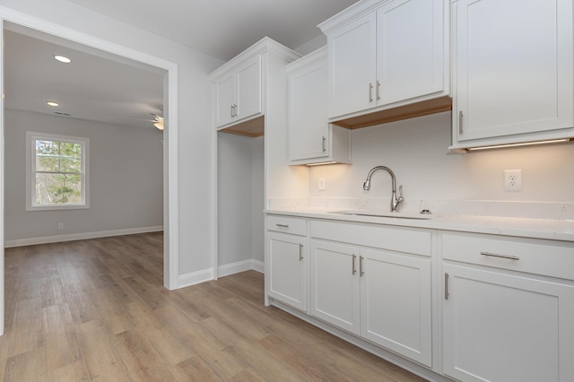 kitchen with light wood-type flooring, ceiling fan, white cabinetry, and sink