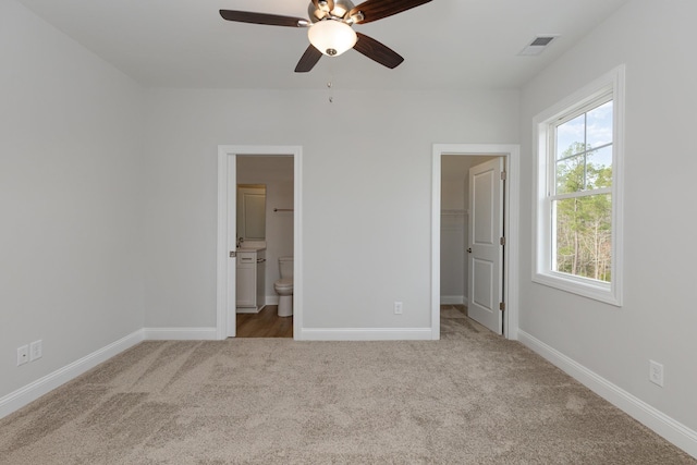 unfurnished bedroom featuring light carpet, connected bathroom, ceiling fan, a closet, and a walk in closet