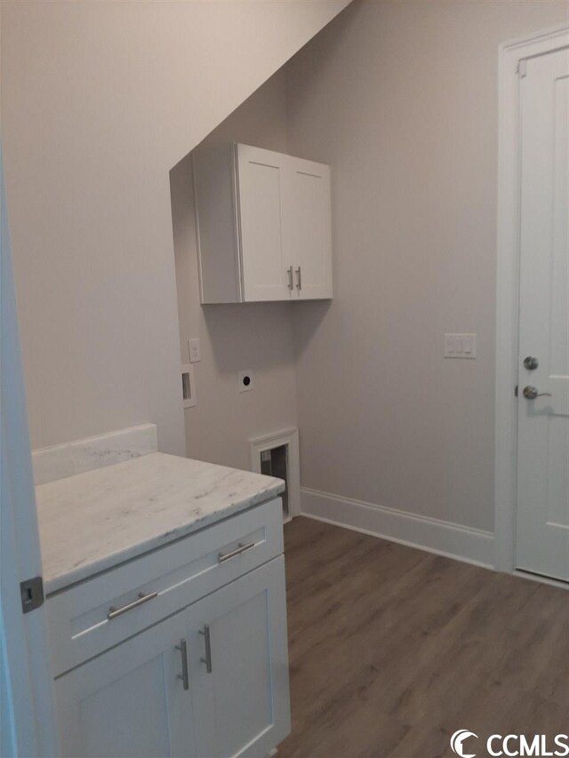 clothes washing area with electric dryer hookup, dark wood-type flooring, and cabinets