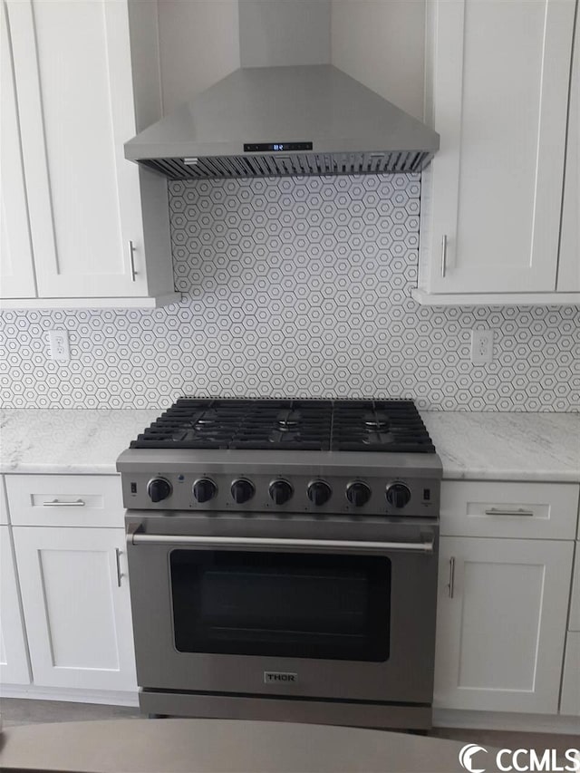 kitchen with wall chimney exhaust hood, white cabinets, light stone countertops, and stainless steel stove