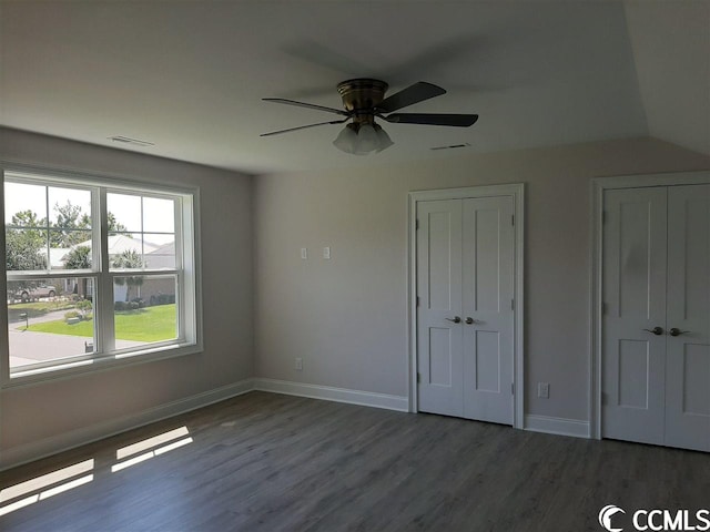 unfurnished bedroom featuring ceiling fan, lofted ceiling, dark wood-type flooring, and multiple closets