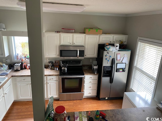 kitchen featuring white cabinets, a textured ceiling, stainless steel appliances, and light wood-type flooring