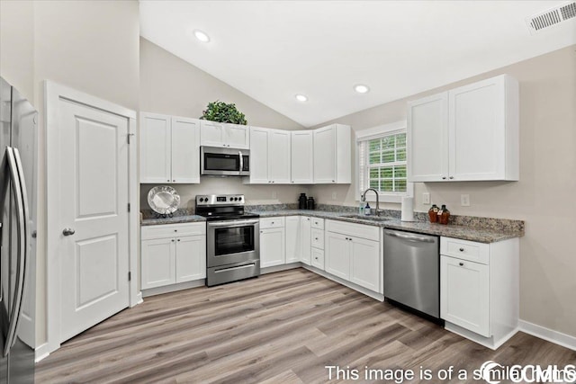 kitchen featuring visible vents, a sink, white cabinetry, stainless steel appliances, and dark stone counters