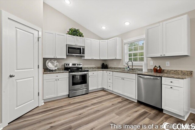 kitchen with appliances with stainless steel finishes, vaulted ceiling, sink, dark stone countertops, and white cabinets