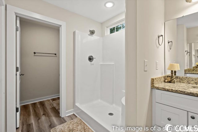 bathroom featuring baseboards, wood finished floors, vanity, and a walk in shower