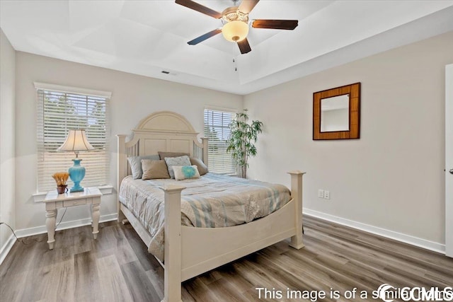 bedroom with a raised ceiling, wood finished floors, visible vents, and baseboards