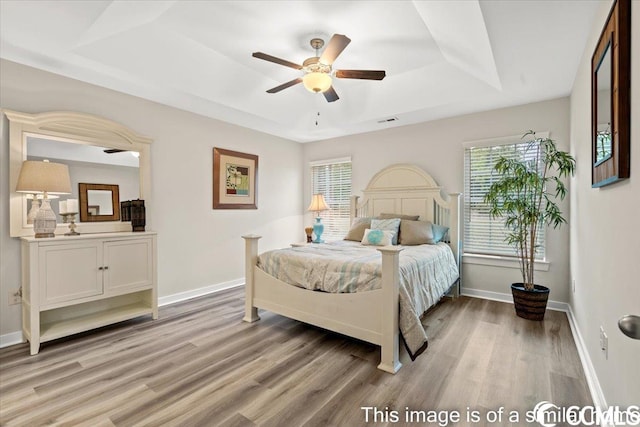 bedroom with a raised ceiling, multiple windows, baseboards, and light wood-type flooring