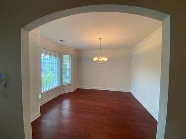 unfurnished dining area featuring dark wood-type flooring, crown molding, and a chandelier