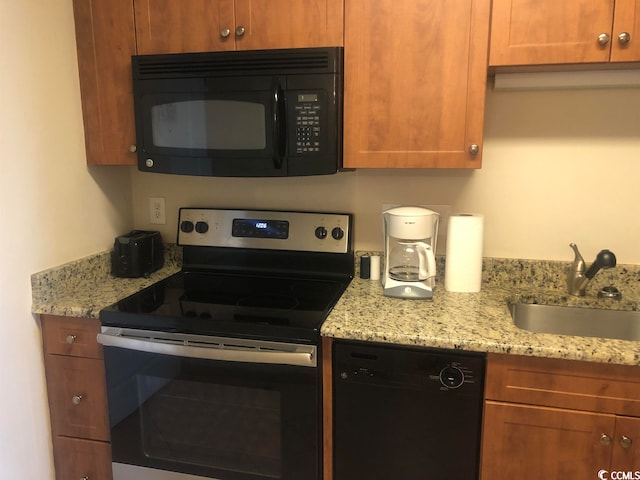 kitchen featuring light stone countertops, black appliances, and sink