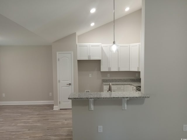 kitchen featuring light stone countertops, kitchen peninsula, decorative light fixtures, a kitchen bar, and white cabinets