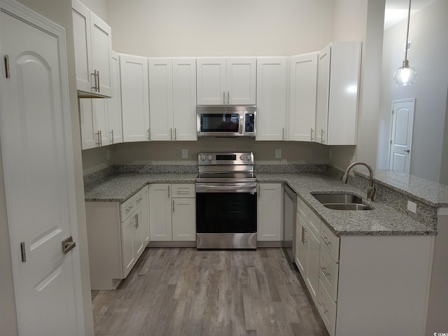 kitchen with sink, kitchen peninsula, pendant lighting, white cabinets, and appliances with stainless steel finishes