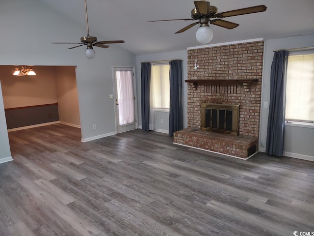 unfurnished living room with dark wood-type flooring, a brick fireplace, vaulted ceiling, and ceiling fan with notable chandelier