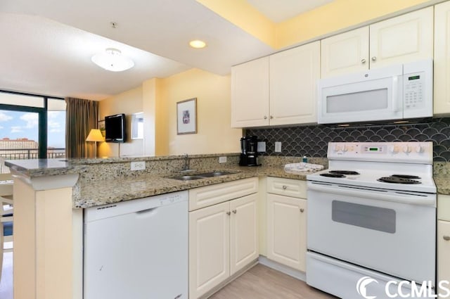 kitchen with kitchen peninsula, white appliances, sink, light stone counters, and backsplash