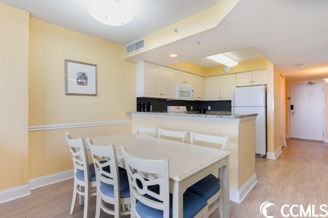 kitchen featuring light stone countertops, white appliances, a kitchen breakfast bar, light hardwood / wood-style flooring, and tasteful backsplash