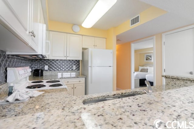 kitchen with range, white cabinets, light stone counters, tasteful backsplash, and white refrigerator