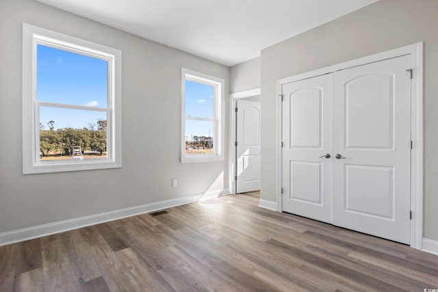 unfurnished bedroom featuring multiple windows, wood-type flooring, and a closet