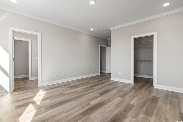 unfurnished bedroom with hardwood / wood-style flooring, ornamental molding, a spacious closet, and a closet