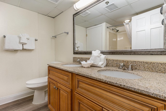 bathroom with hardwood / wood-style flooring, vanity, a paneled ceiling, and toilet