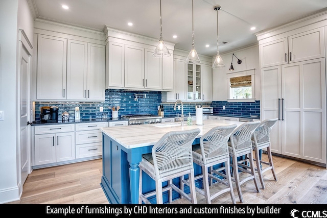 kitchen with light hardwood / wood-style floors, an island with sink, white cabinets, tasteful backsplash, and a breakfast bar area