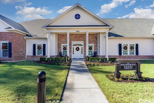 greek revival house featuring a shingled roof, a front yard, and brick siding