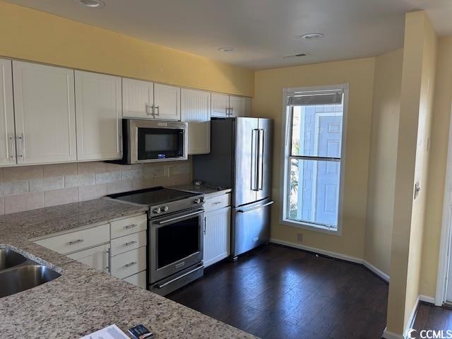 kitchen featuring backsplash, dark wood-type flooring, white cabinets, appliances with stainless steel finishes, and light stone counters