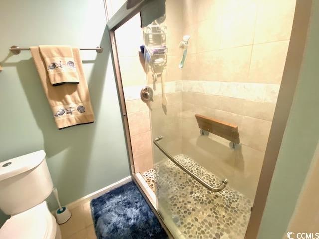 bathroom featuring tile patterned floors, a shower with door, and toilet