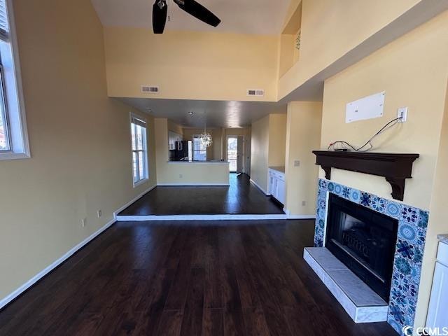 unfurnished living room with a tile fireplace, ceiling fan, a towering ceiling, and dark hardwood / wood-style floors