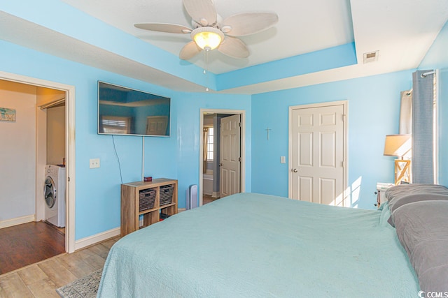 bedroom with washer / clothes dryer, ceiling fan, a tray ceiling, and hardwood / wood-style flooring