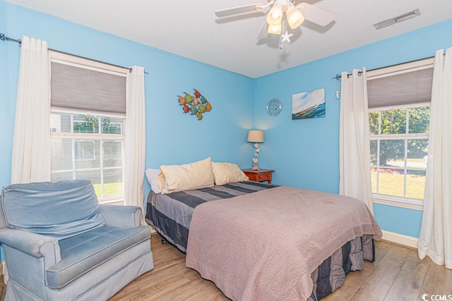 bedroom with light wood-type flooring, ceiling fan, and multiple windows