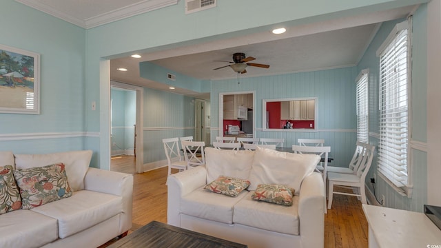 living area featuring a ceiling fan, wood finished floors, visible vents, and crown molding