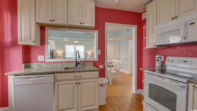 kitchen featuring light stone counters, light wood-style flooring, white appliances, a sink, and baseboards