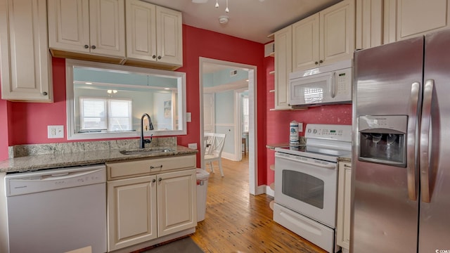 kitchen featuring white appliances, baseboards, light stone counters, light wood-style floors, and a sink