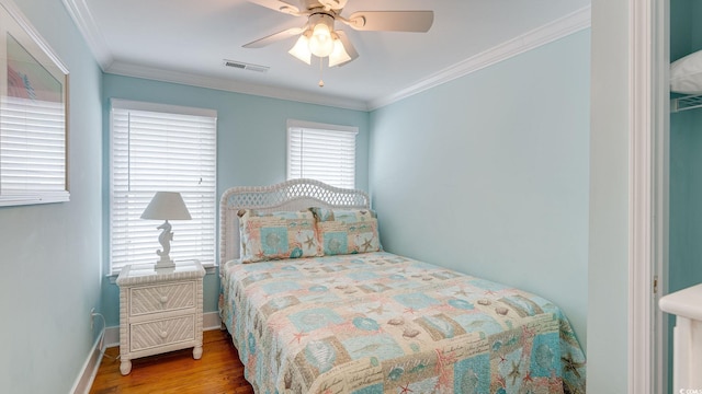 bedroom with baseboards, wood finished floors, visible vents, and crown molding