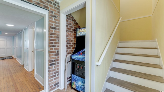 staircase with brick wall and hardwood / wood-style floors