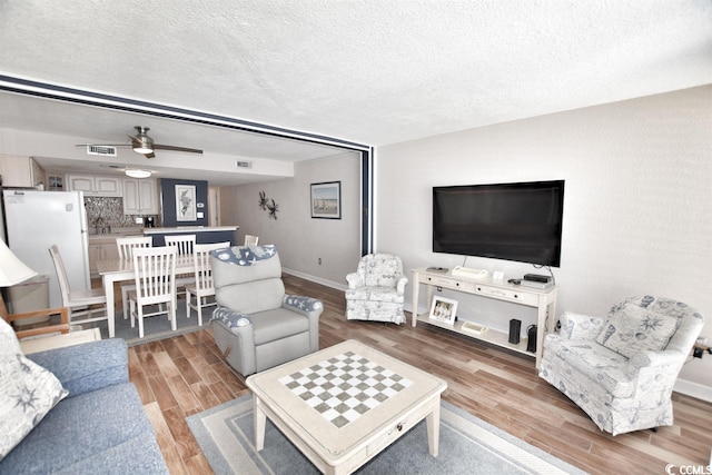 living room with light hardwood / wood-style floors, a textured ceiling, and ceiling fan