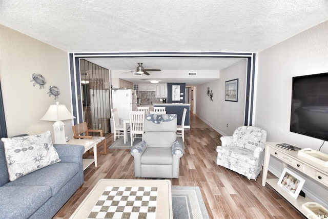 living room with a textured ceiling, ceiling fan, and wood-type flooring