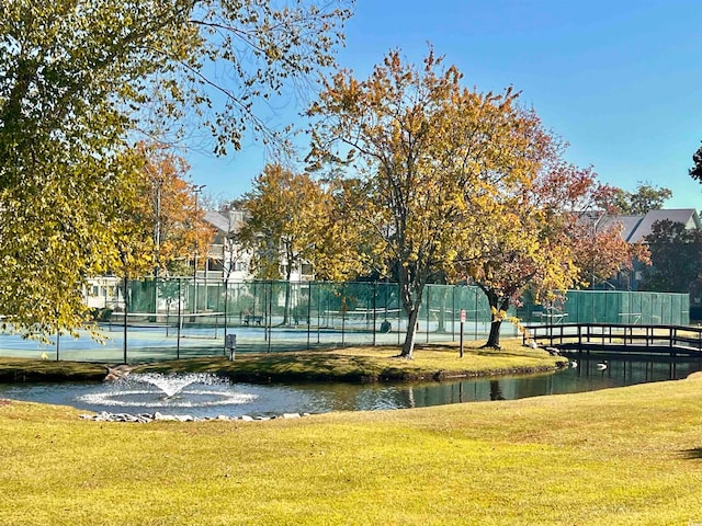 view of community featuring a water view, a lawn, and tennis court