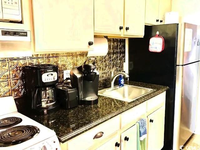 kitchen with white electric range oven, decorative backsplash, white cabinetry, a sink, and dark stone countertops