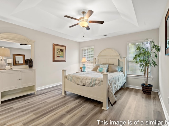 bedroom featuring multiple windows, a raised ceiling, light wood-type flooring, and ceiling fan