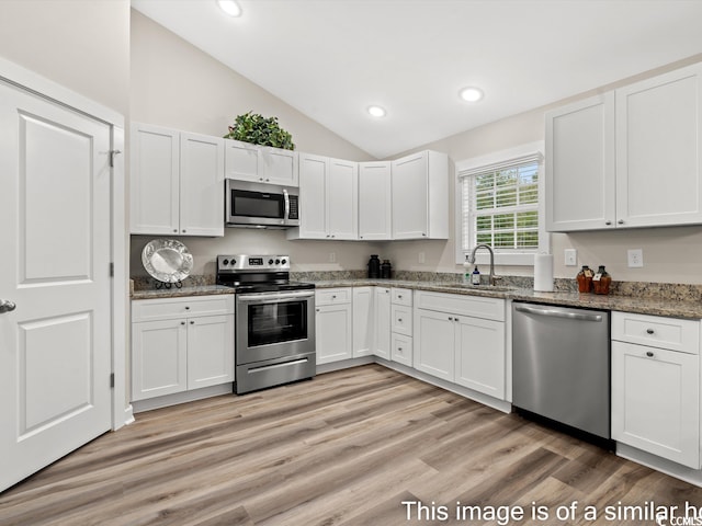 kitchen with sink, appliances with stainless steel finishes, vaulted ceiling, and white cabinetry