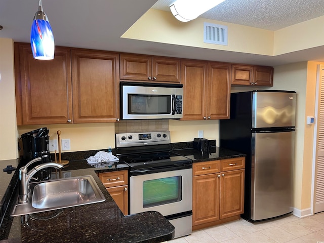 kitchen with stainless steel appliances, dark stone counters, sink, pendant lighting, and light tile floors