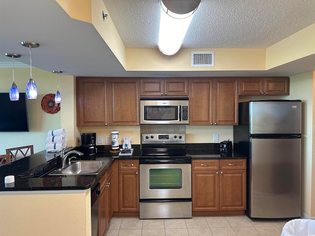 kitchen with appliances with stainless steel finishes, sink, light tile flooring, kitchen peninsula, and pendant lighting